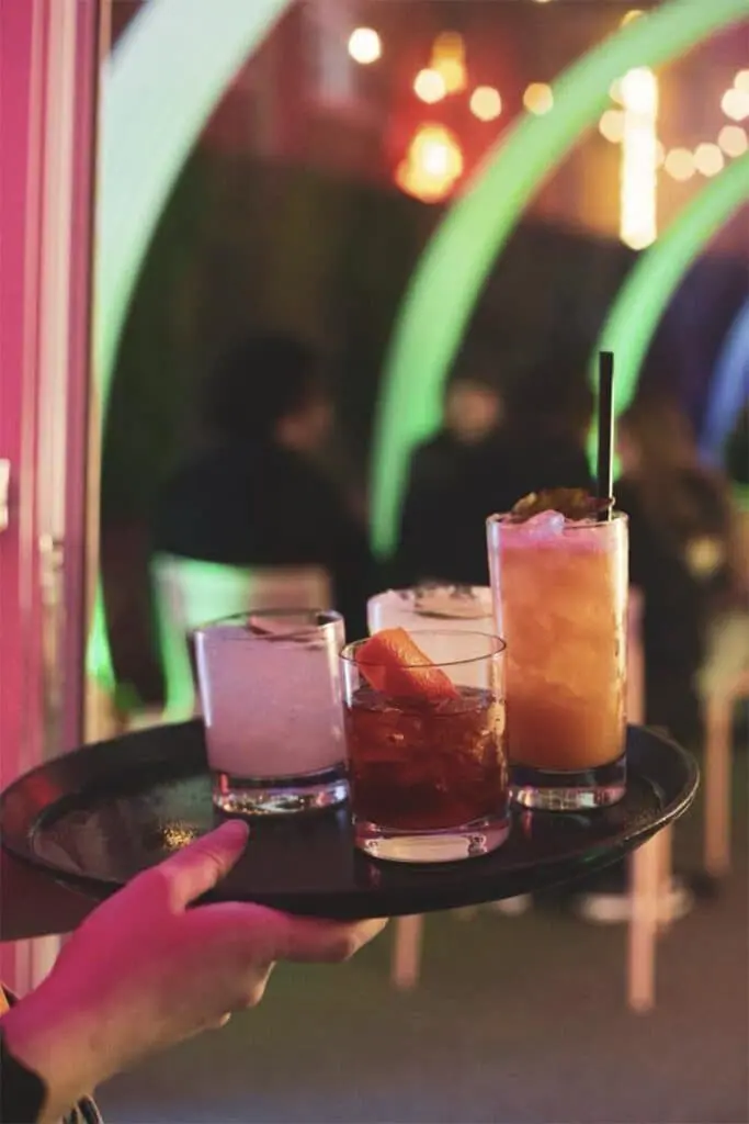Colorful cocktails served on a tray at a lively bar or nightclub.