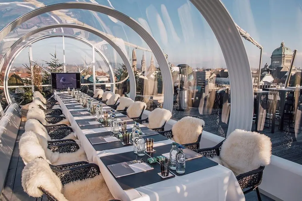 Rooftop dining area with a long table and cozy chairs, city skyline views, and modern design décor.