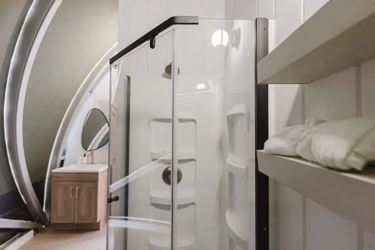 Modern shower enclosure with glass doors, bathroom vanity, and storage shelves, showcasing bathroom sanitation products.