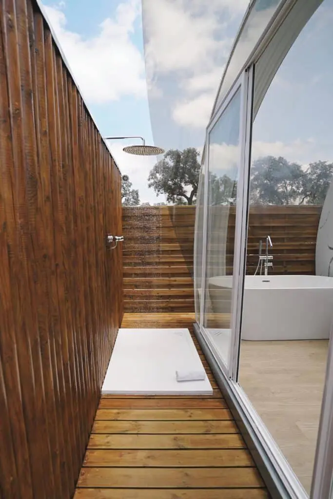 Outdoor shower and bathtub in modern bathroom with wooden walls and glass enclosure, eco-friendly design, relaxing outdoor bathing area.