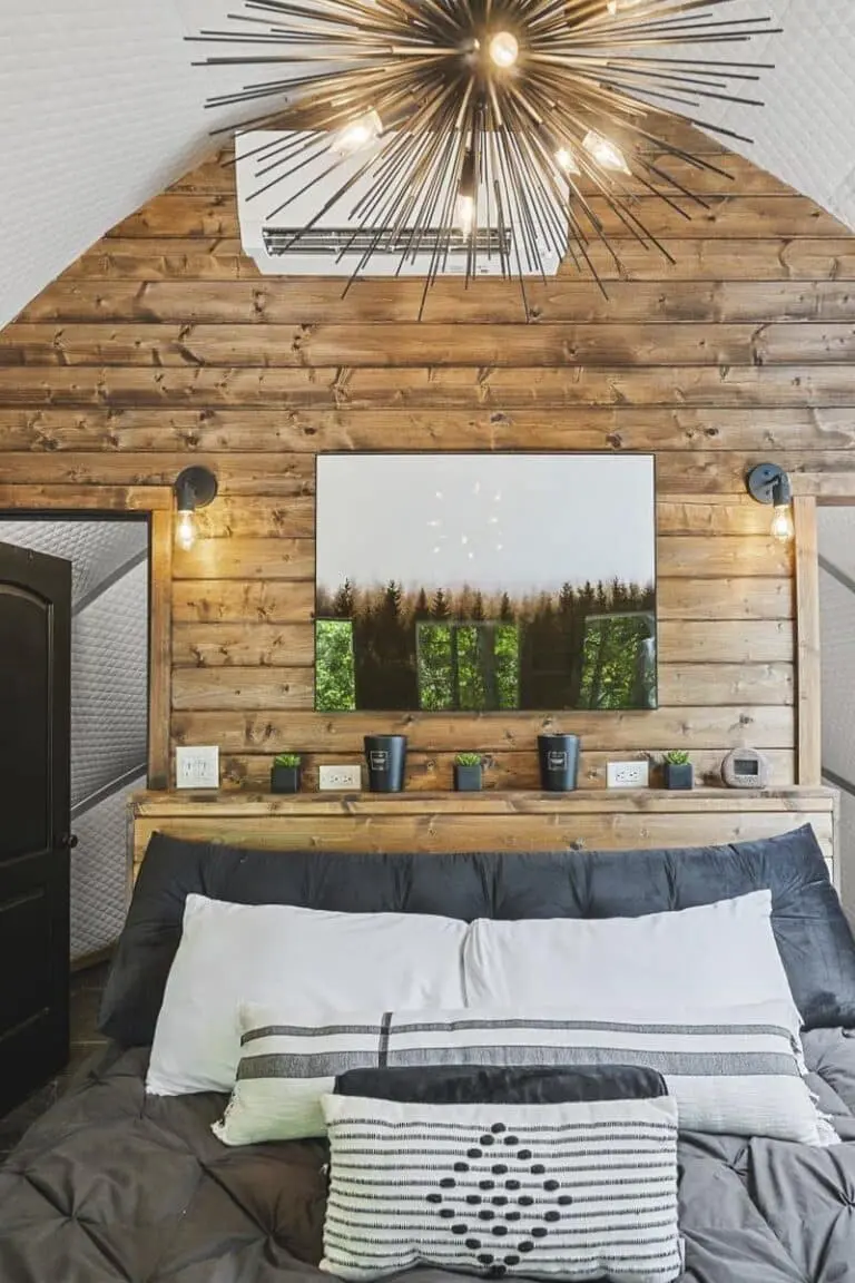 Modern rustic bedroom with wooden accent wall and stylish lighting fixtures.