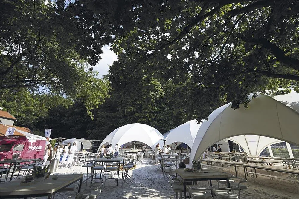 Modern outdoor event setup with white tents, tables, and a food truck for gatherings and celebrations.