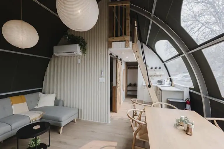 Modern tiny house interior with cozy seating and kitchen area, eco-friendly design, large windows, and efficient space utilization.