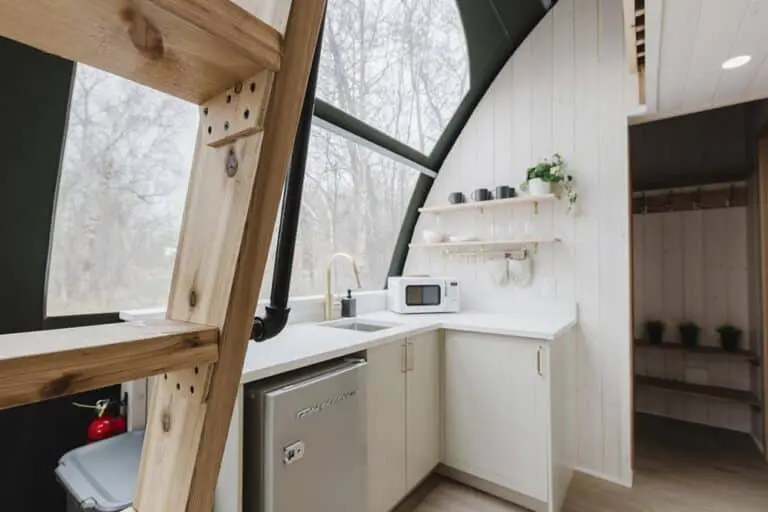 Bright modern tiny home kitchen with skylight and white cabinetry, cedar accents, and compact appliances.