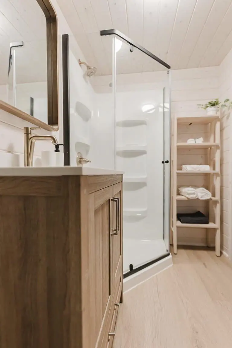 Modern bathroom with wooden vanity and glass shower enclosure, showcasing quality fixtures and storage solutions.