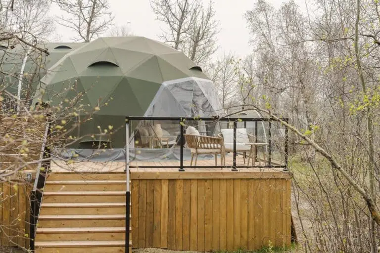 Geodesic dome cabin on wooden deck surrounded by trees, outdoor furniture, and railing, eco-friendly glamping retreat.