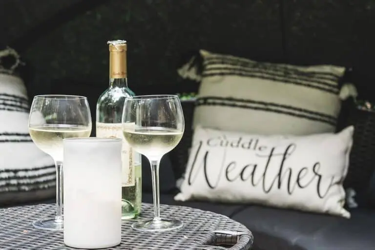 Elegant outdoor setting with wine glasses, a bottle of white wine, and cozy cushions for relaxation.