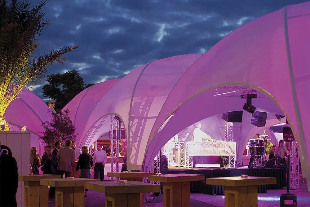 Vibrant outdoor event space with illuminated pink tent structures and live DJ performance at twilight.