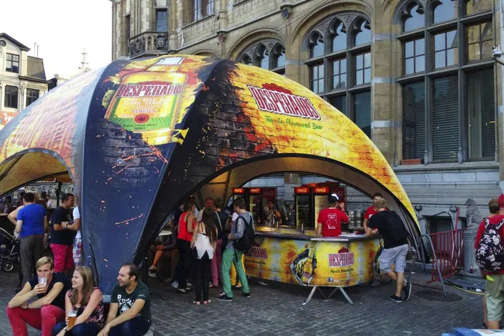 Vibrant Desperados beer tent at outdoor event with people enjoying drinks and socializing.