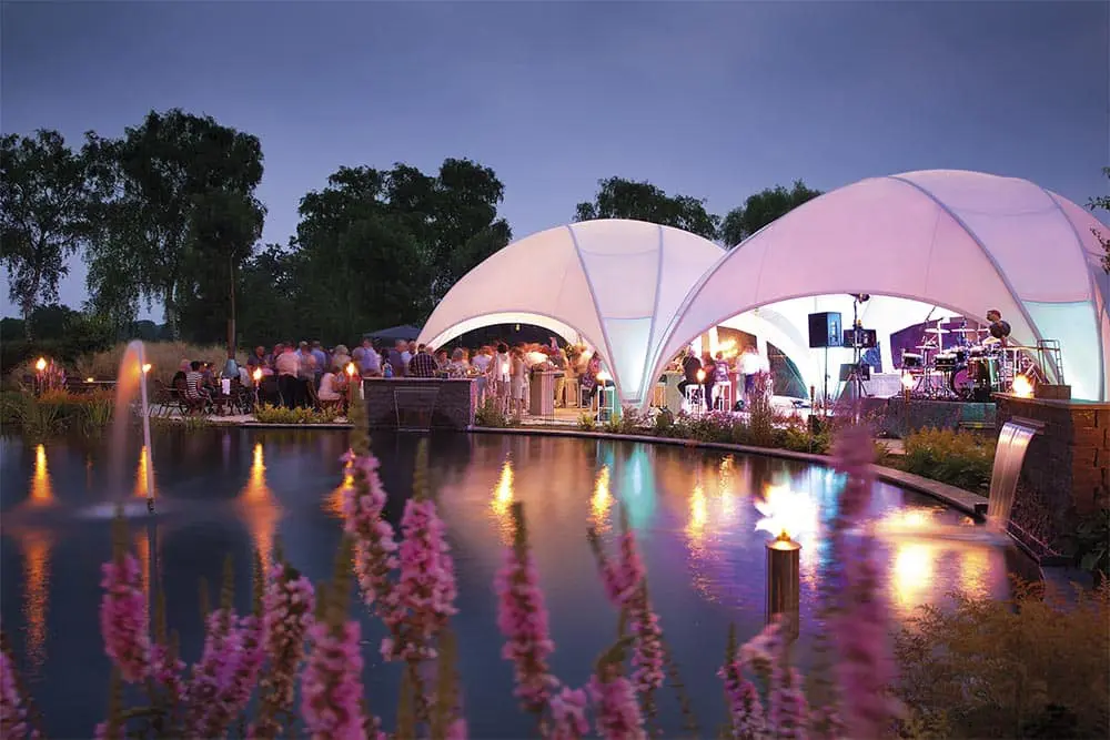 Elegant outdoor event at dusk with illuminated tents, live music, and a reflecting pool at EJH Distribution.