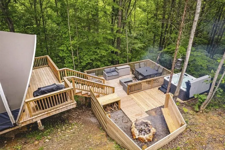 Spacious outdoor wooden deck with seating area and hot tub surrounded by lush green trees.