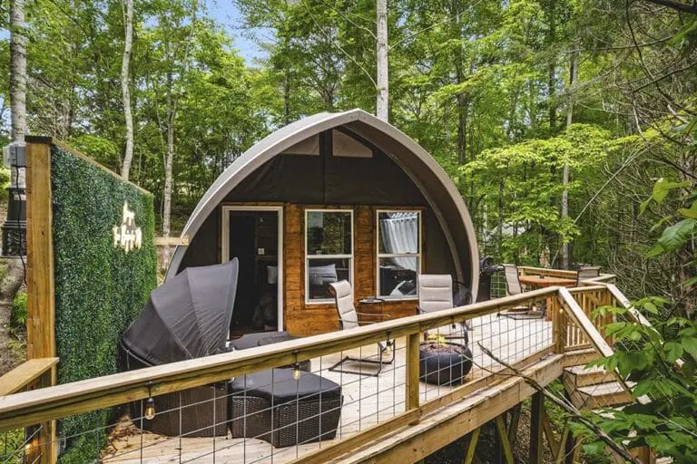 Cozy glamping cabin with outdoor deck nestled among lush green trees, perfect for nature retreats and outdoor living.