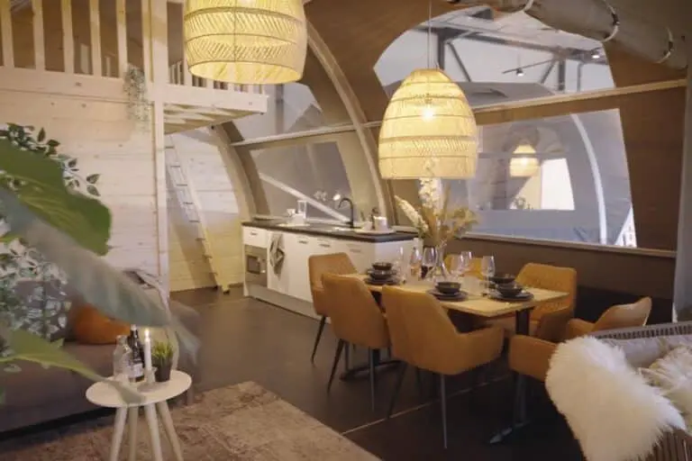 Cozy modern tiny house interior with dining area and kitchen, warm lighting and natural wood decor.