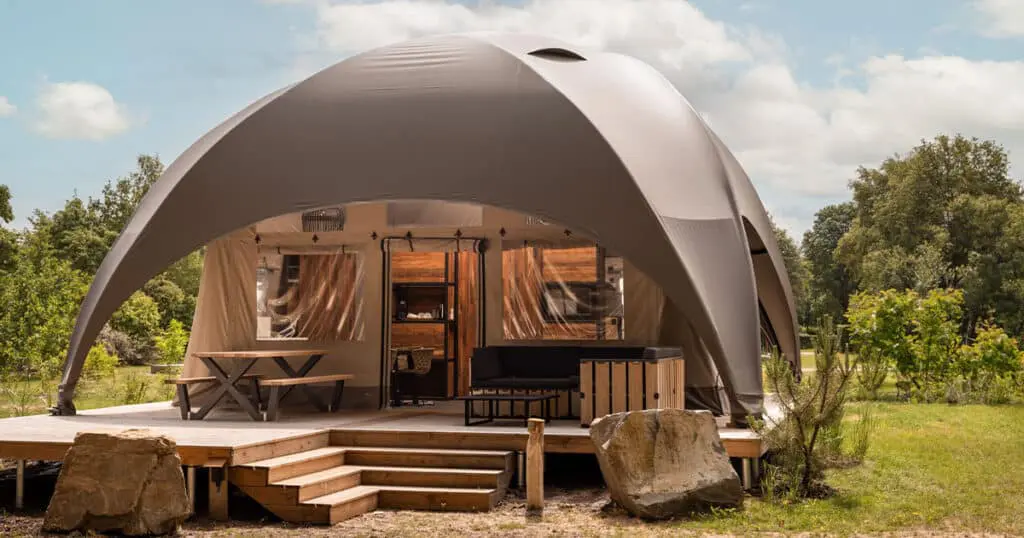 Yurt-style eco-friendly glamping tent with outdoor wooden deck and cozy seating area in nature.
