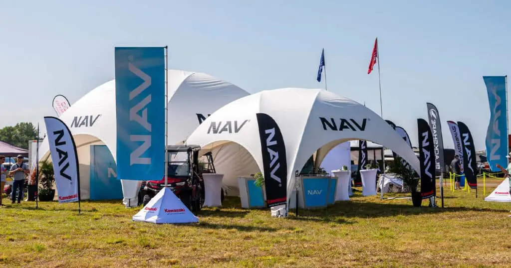 Nav team on display at outdoor event with branded tents and flags, showcasing Kawasaki and NAV products.
