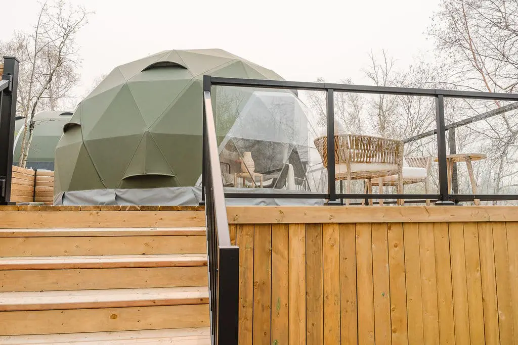 Geodesic dome outdoor seating area on a wooden deck with furniture and glass railing, ideal for eco-friendly backyard relaxation.