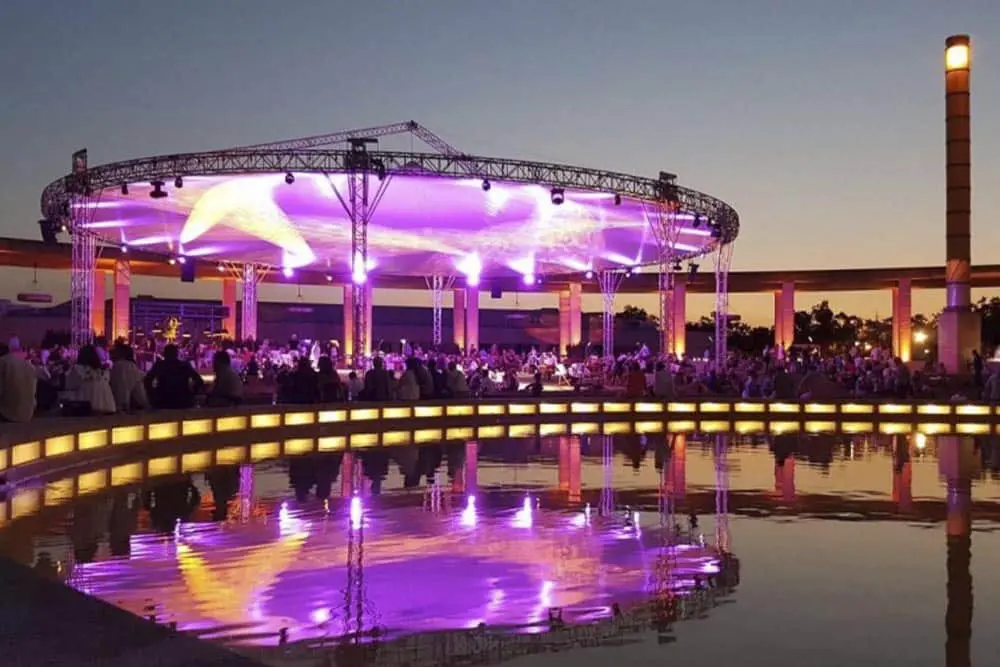 Vibrant outdoor event at sunset with stage lighting and audience near water reflection, showcasing event lighting solutions.