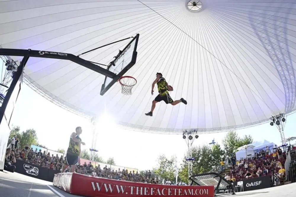 Aerial view of basketball game under a large domed roof with players performing slam dunks.