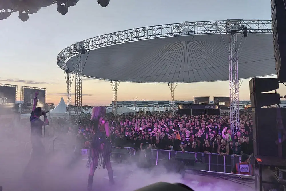 Vibrant outdoor concert with large crowd under a modern canopy at sunset.