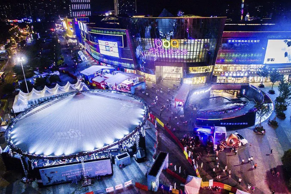 Brightly lit shopping mall and entertainment complex at night with vibrant neon signs and crowd activities, showcasing retail and leisure spaces.
