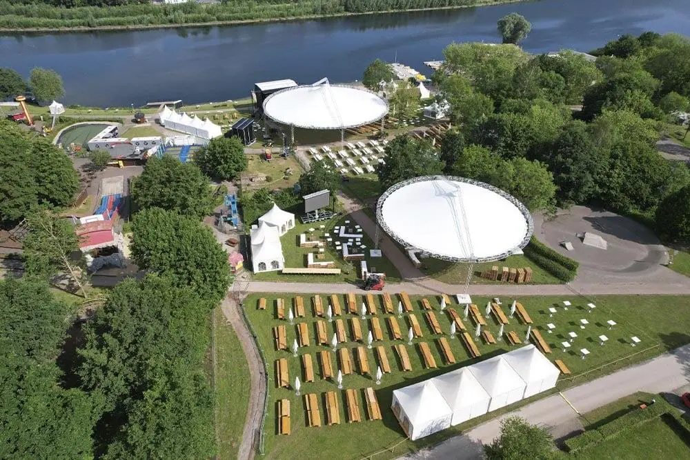 Aerial view of event setup at EJH Distribution near a river with tents, stages, and outdoor seating.