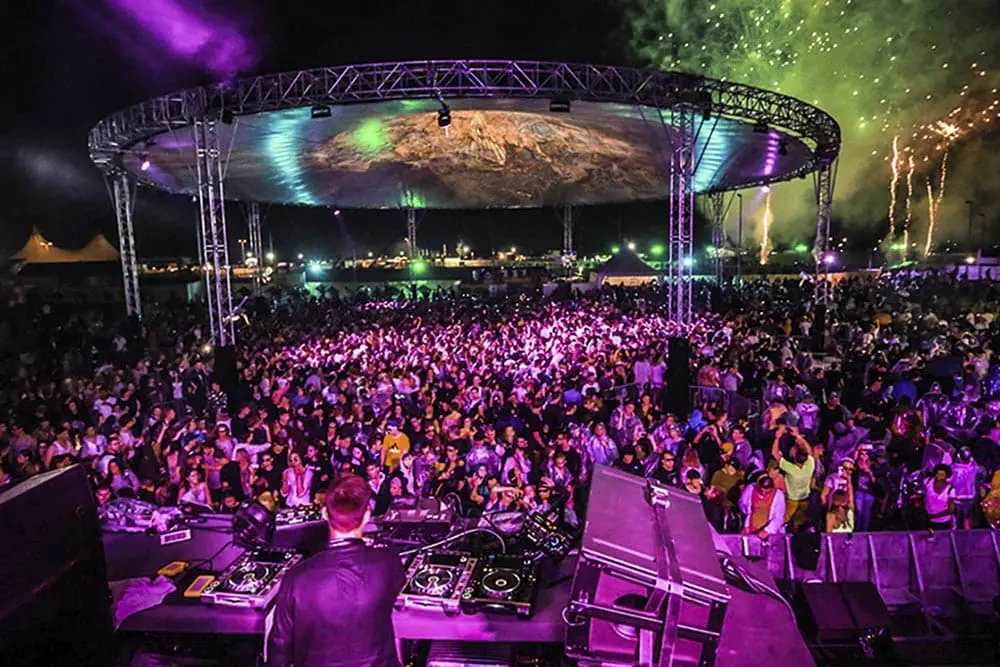 Vibrant night festival with DJ performing at large outdoor concert with colorful lights and fireworks.
