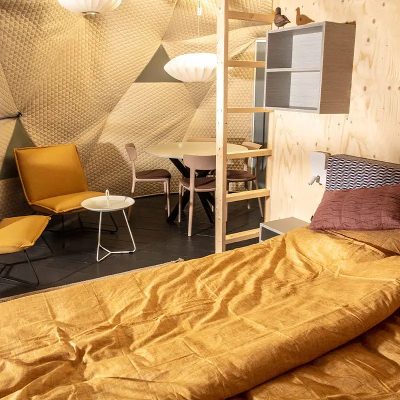 Cozy modern bedroom with seating area and wooden accents, stylish furniture, warm lighting, and textured wall design.