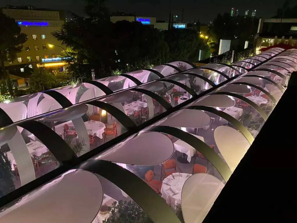 Elegant rooftop restaurant with retractable glass canopy at night, offering a sophisticated dining experience.