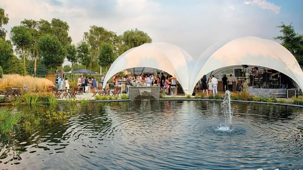 Elegant outdoor event with modern white tents, waterfront views, live music, and social gatherings.