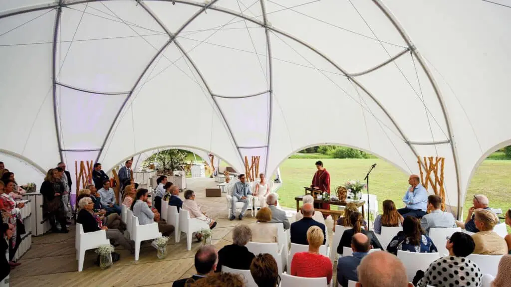 Vow renewal ceremony inside a modern outdoor wedding tent with guests and officiant.