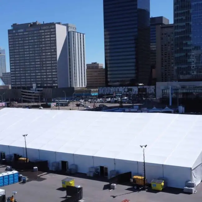 Large white event tent set up in downtown urban area with modern skyscrapers in the background.