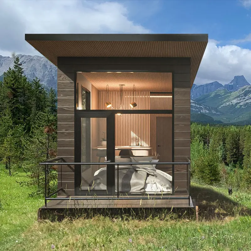 Modern tiny cabin in a lush mountain landscape with expansive windows and wooden exterior.