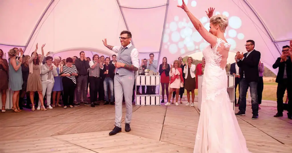 Happy wedding celebration with dancing bride and groom at outdoor event under a unique pavilion.