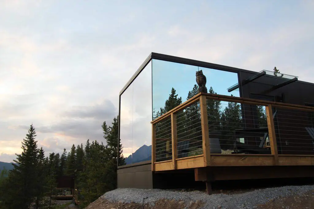 Modern glass-walled mountain retreat featuring sleek design and panoramic views, with a spacious wooden balcony, perfect for outdoor relaxation amid nature.