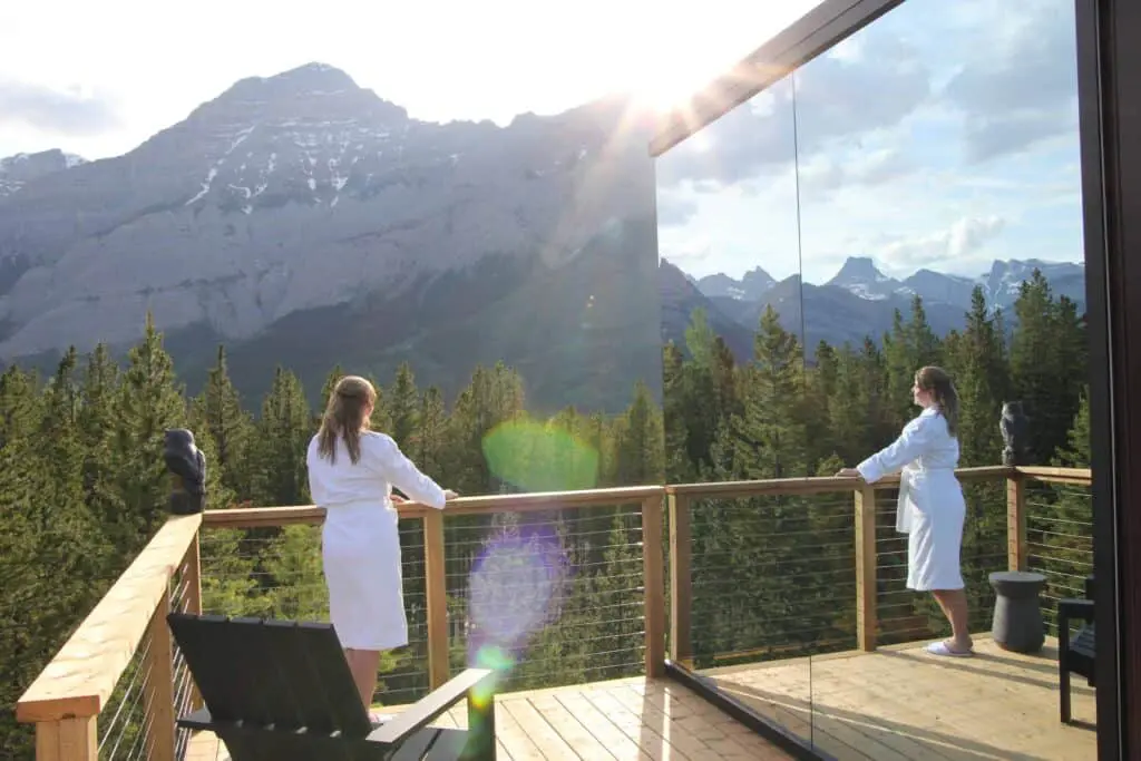 Breathtaking mountain view from a balcony at EJH Distribution, showcasing serene pine forests and snow-capped peaks with two women in white robes enjoying the tranquil scenery.