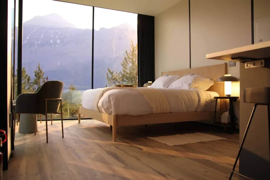 Modern hotel bedroom with large window overlooking mountain landscape, cozy bedding, stylish lighting, and contemporary furnishings, highlighting comfort and scenic views.