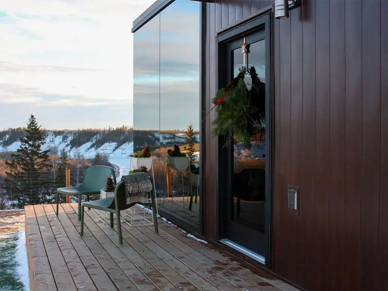 Modern outdoor deck with seating area and glass door, overlooking snow-covered landscape, showcasing stylish design and winter scenery.
