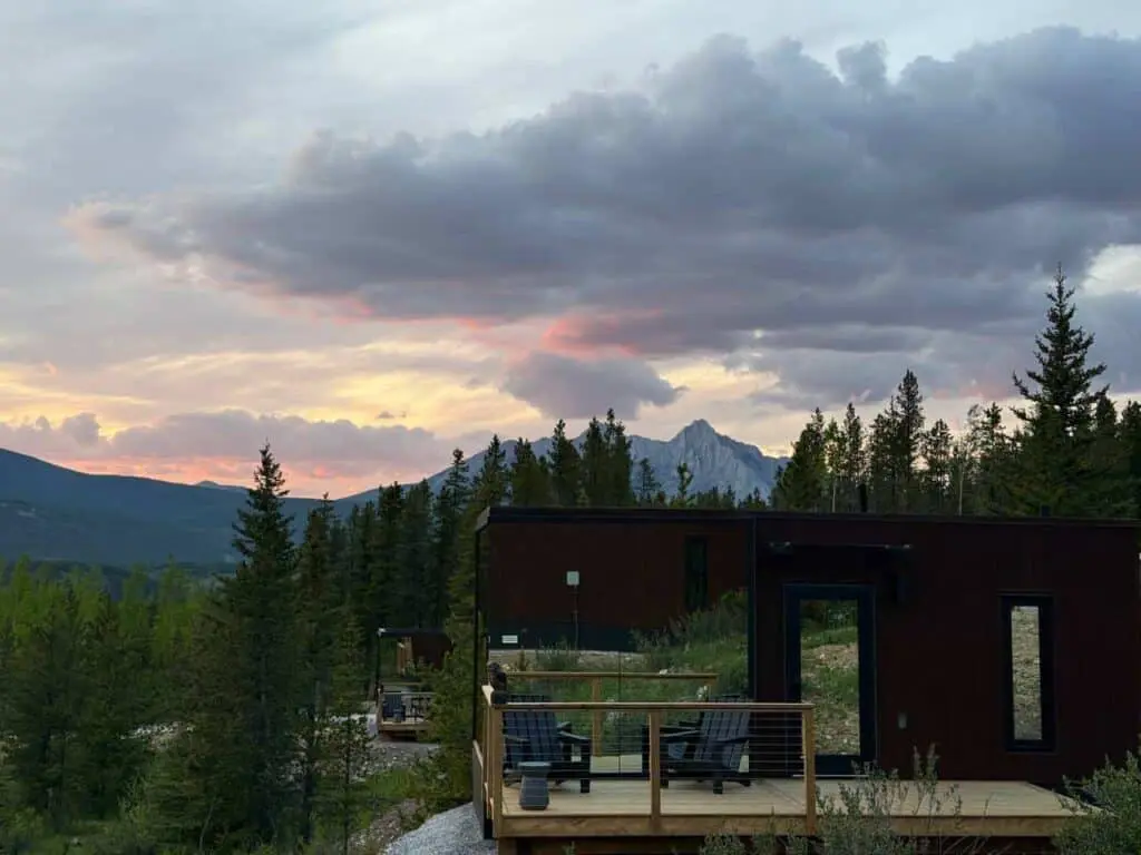 Modern tiny home with a mountain view, outdoor deck, and lush forest surroundings at sunset. Perfect for nature lovers seeking eco-friendly living spaces.
