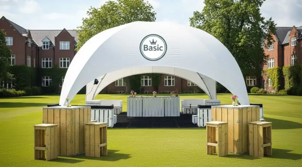A stylish outdoor event tent with a modern design, white fabric, and the word "Basic" printed on it, set up on a lush green lawn with surrounding buildings and trees for a garden party or celebration.