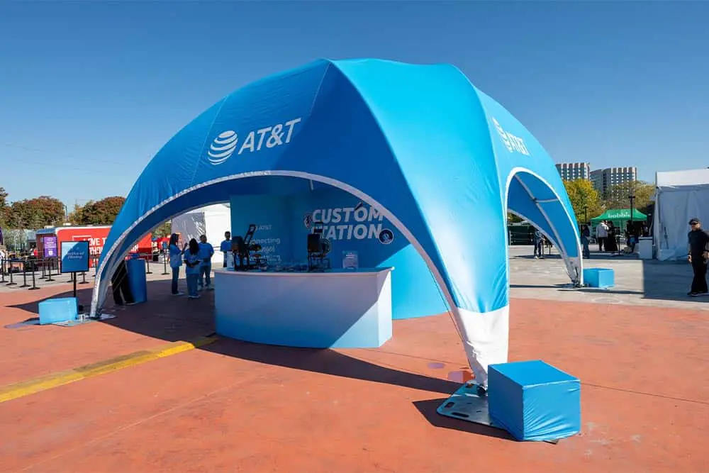 A large blue AT&T promotional tent at an outdoor event with seating and registration area, showcasing branding and customer engagement.