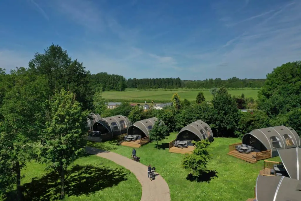 Aerial view of modern glamping eco pods nestled in lush greenery, surrounded by trees and open fields, offering a unique outdoor accommodation experience.