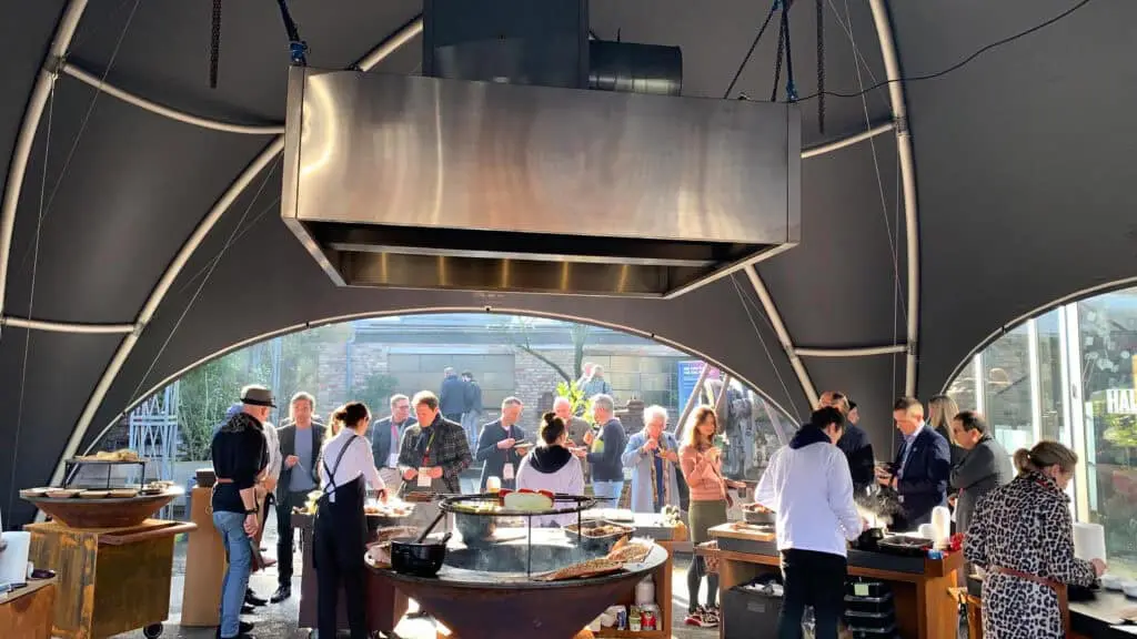 Vibrant outdoor hospitality event with guests enjoying fresh food and drinks under a modern tent structure.