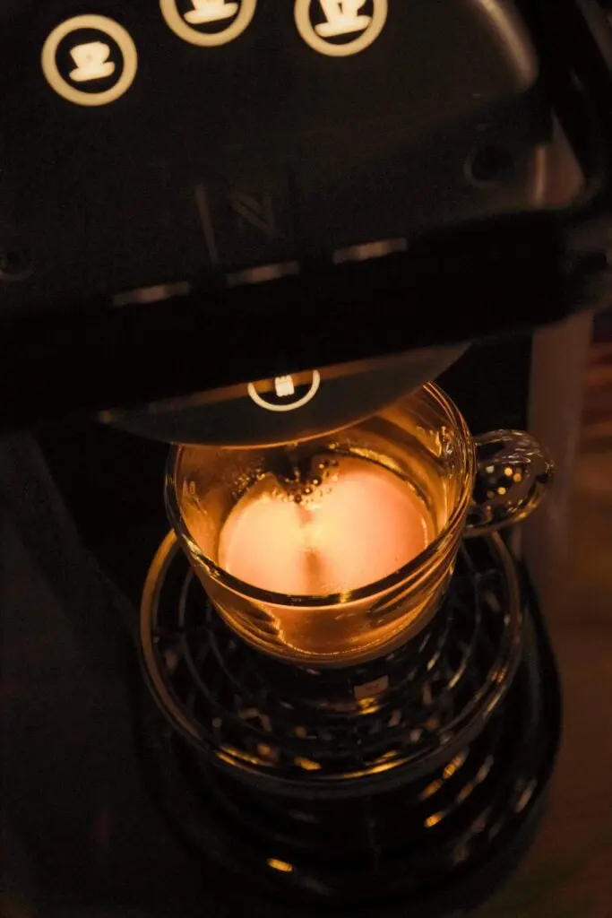 Coffee machine pouring hot water into a glass cup with brewed coffee.