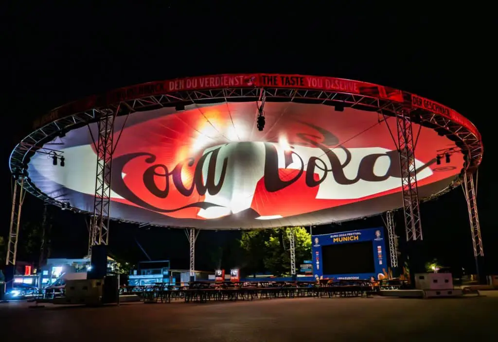 Large Coca-Cola branded stage setup at night for brand activation event, illuminated with vibrant lighting and digital screens, creating an engaging atmosphere.