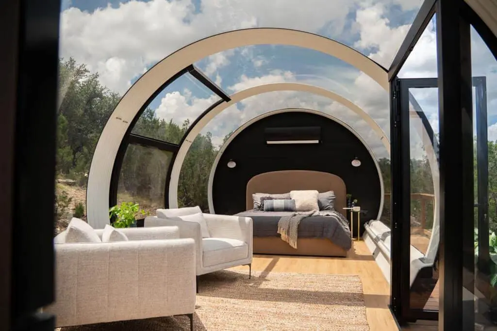 Bright, stylish bedroom with glass walls, circular architecture, and comfortable bed in a scenic outdoor setting.