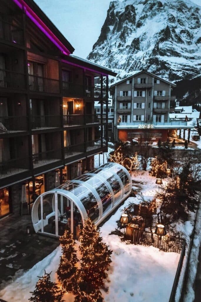 Modern ski resort hotel with heated indoor pool and festive holiday lighting nestled in snowy mountain landscape.