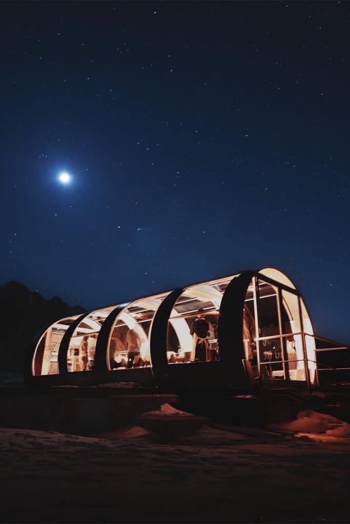 Bright moonlit night with stars above a glass-enclosed mountain cabin.