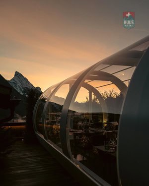 Futuristic glass cabin with mountain view at sunset for innovative hospitality experience.