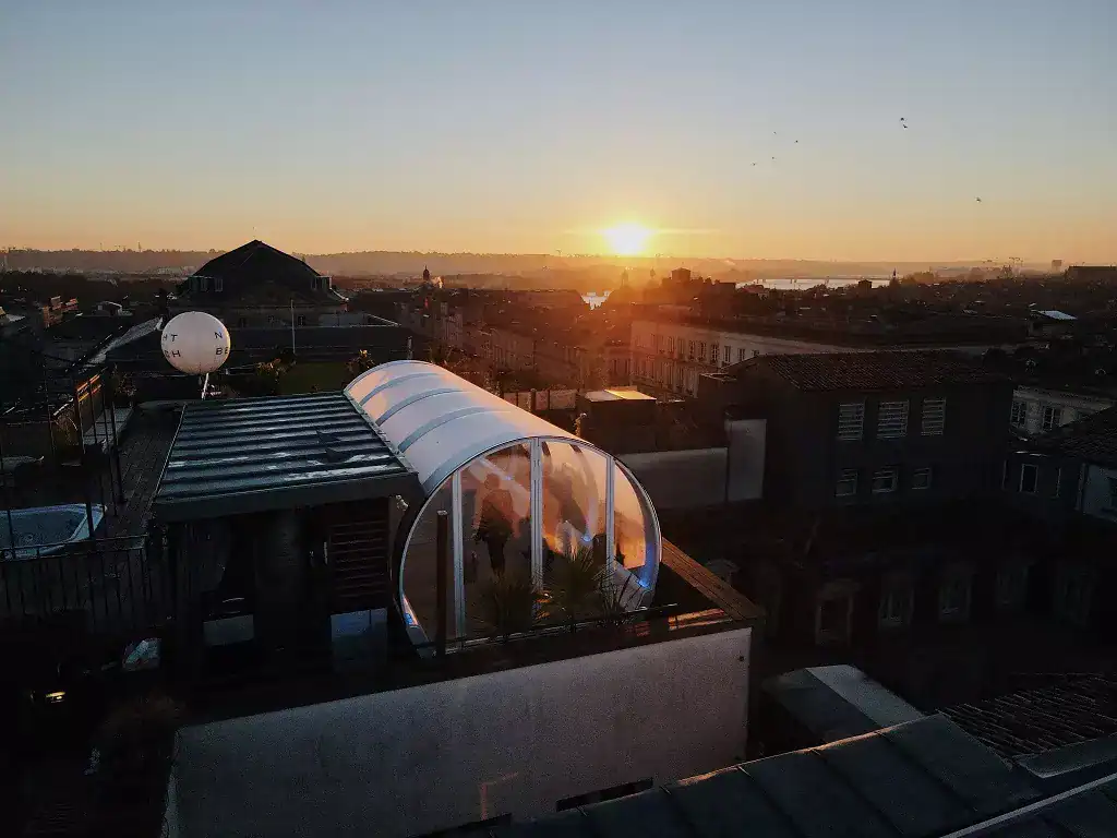 Urban rooftop during sunset with greenhouse and water tower, San Francisco cityscape, EJH Distribution logo, modern architecture, city view, evening light, scenic horizon, skyline.
