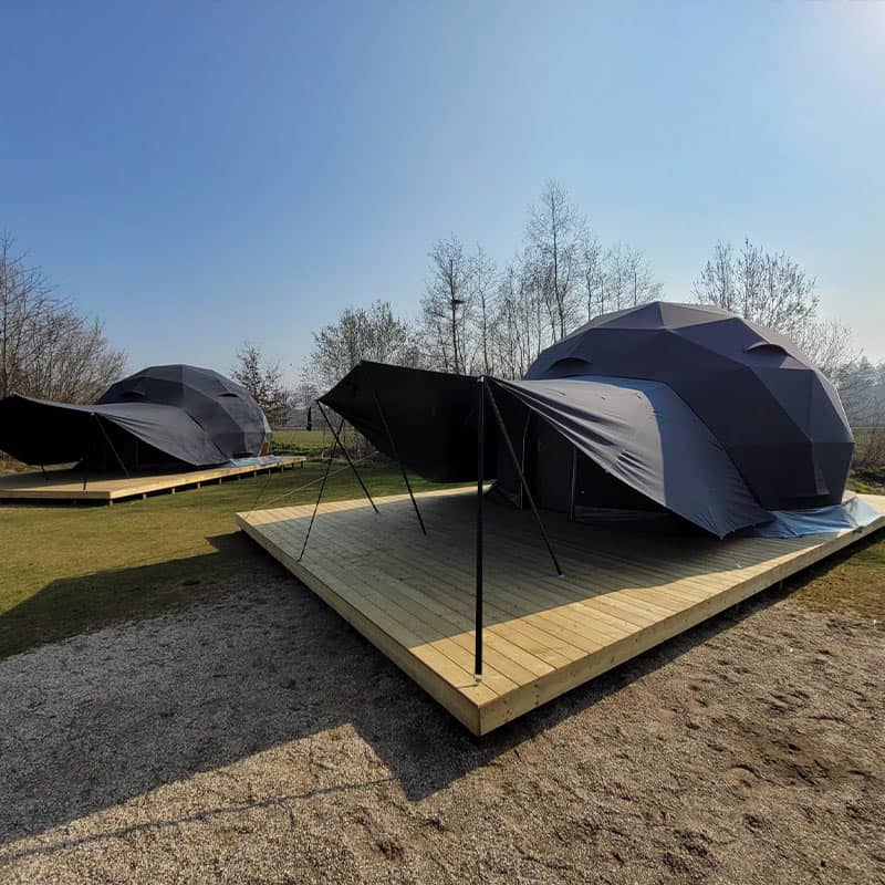 Black outdoor tents on wooden decks for camping and events, outdoors in a natural setting with trees and clear blue sky.